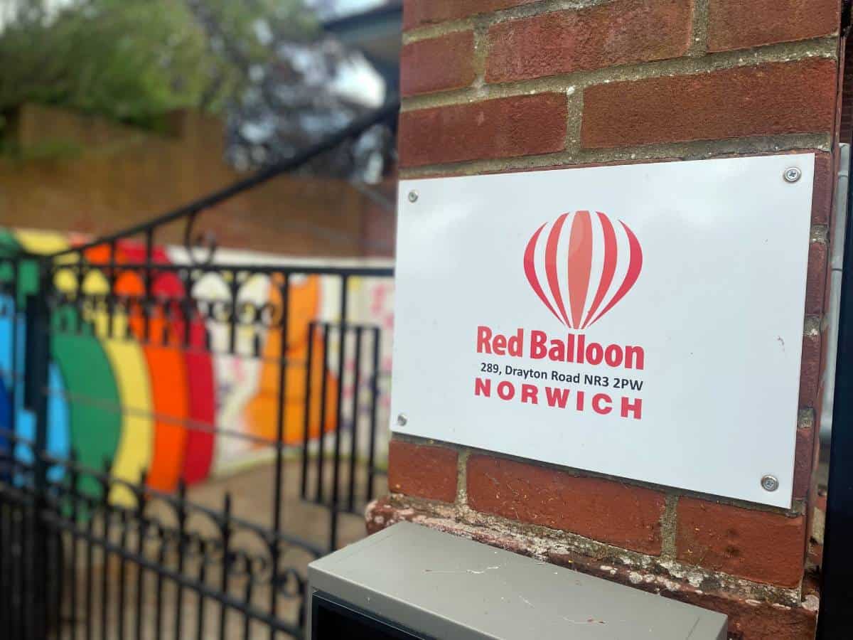 Red Balloon sign, Norwich, colourful fence background.
