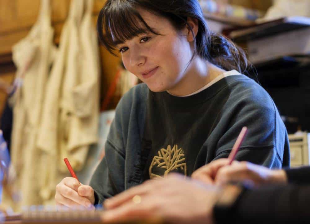 Woman writing in workshop with focus and smile.