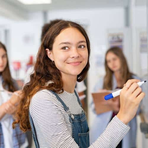 Smiling student with pen in a classroom setting.